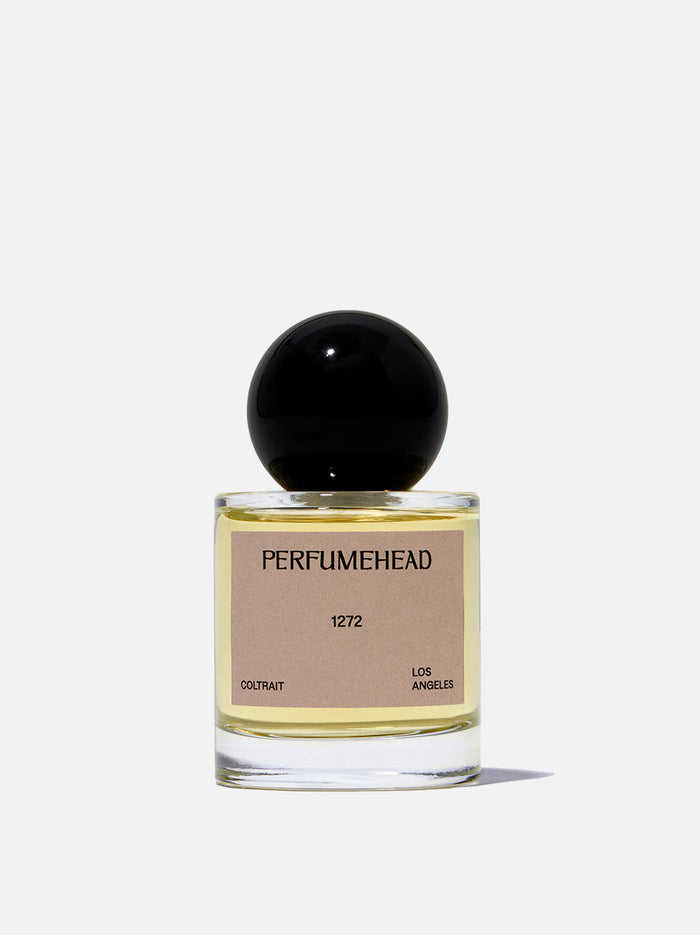 A bottle of Perfumehead 1272 Coltrait, featuring a clear glass bottle with pale yellow liquid, a beige label, and a glossy black spherical cap, set against a white background.