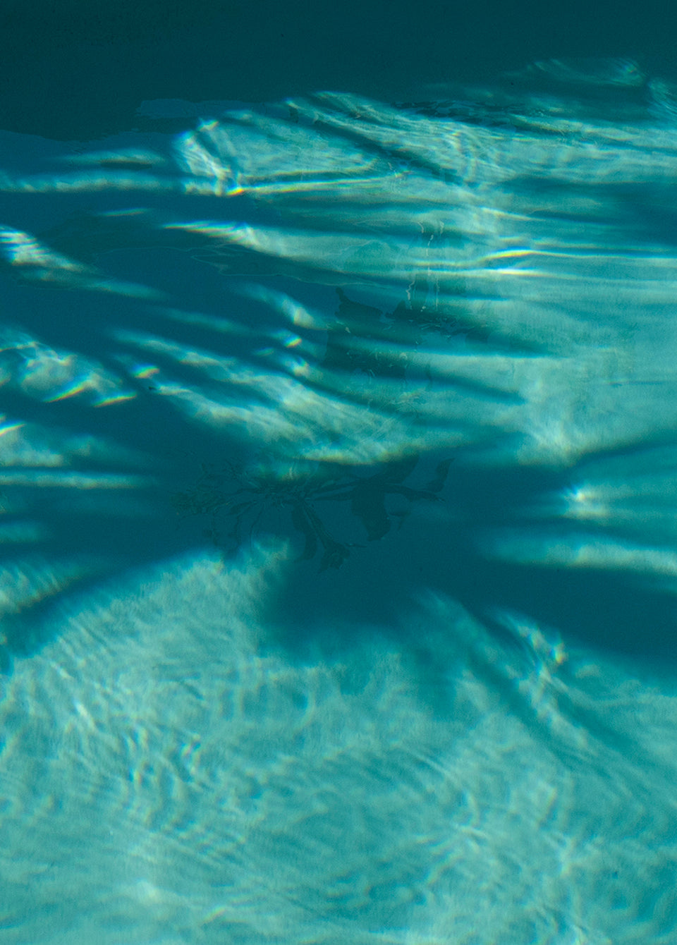 Underwater photograph of clear turquoise water with ripples and dappled light shadows across the pool floor.