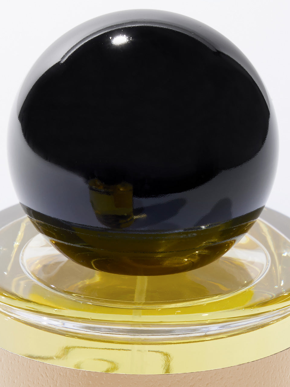 A close-up of a glossy black spherical bottle cap resting on a clear circular base with yellow liquid visible inside, set against a plain white background.