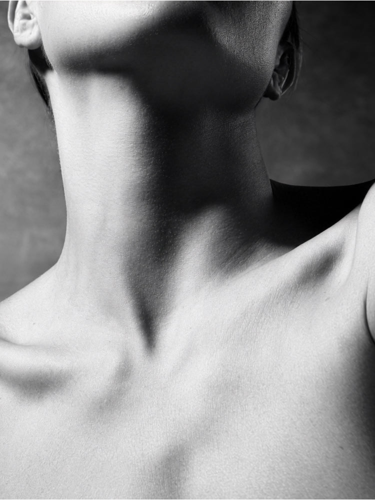 Black and white close-up photograph of a person's neck, jawline, and upper chest, with dramatic directional lighting and soft shadow.