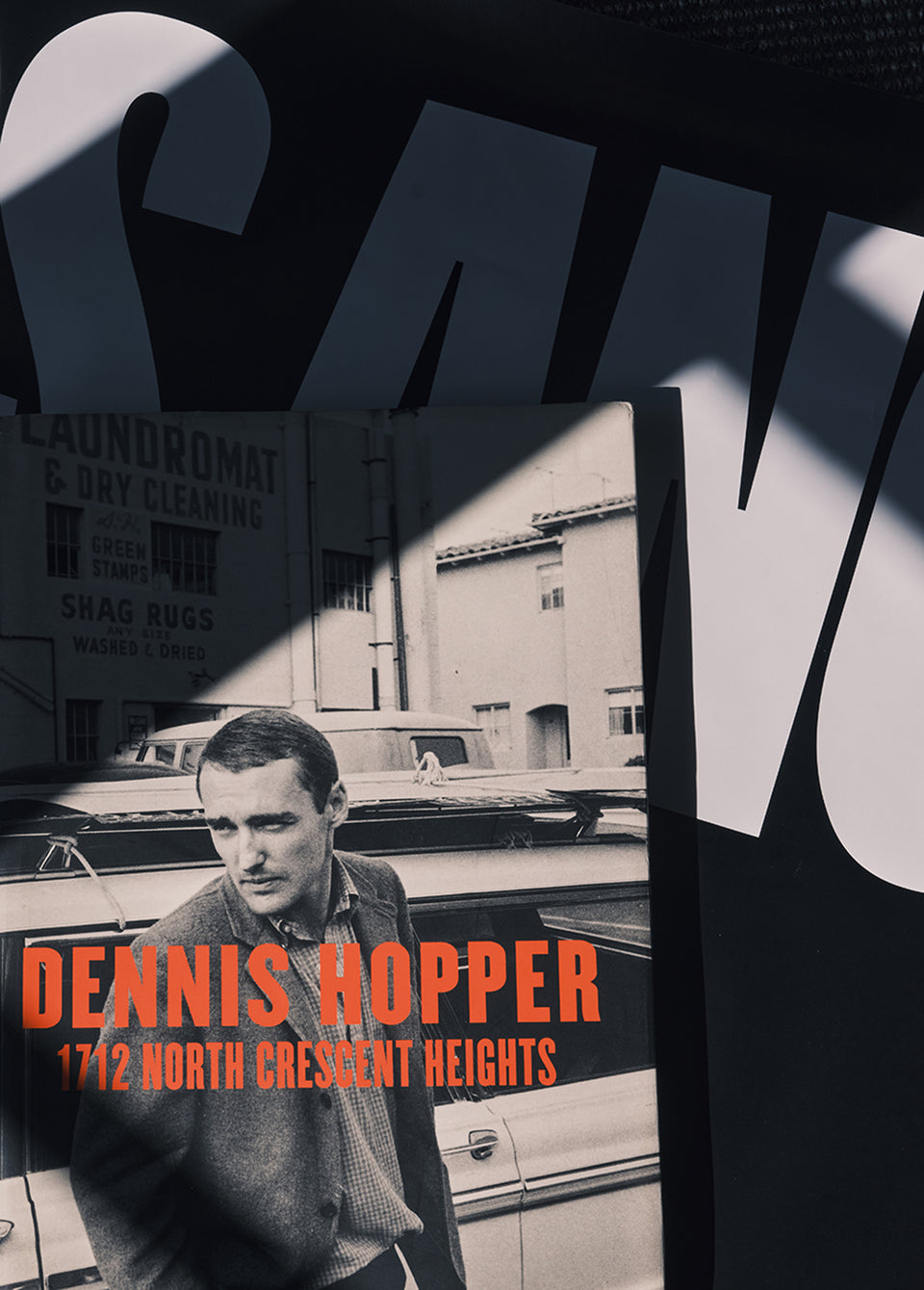 A book cover for 'Dennis Hopper: 1712 North Crescent Heights' is shown in a stylized, high-contrast black-and-white street photograph layout with large white letters in the background.