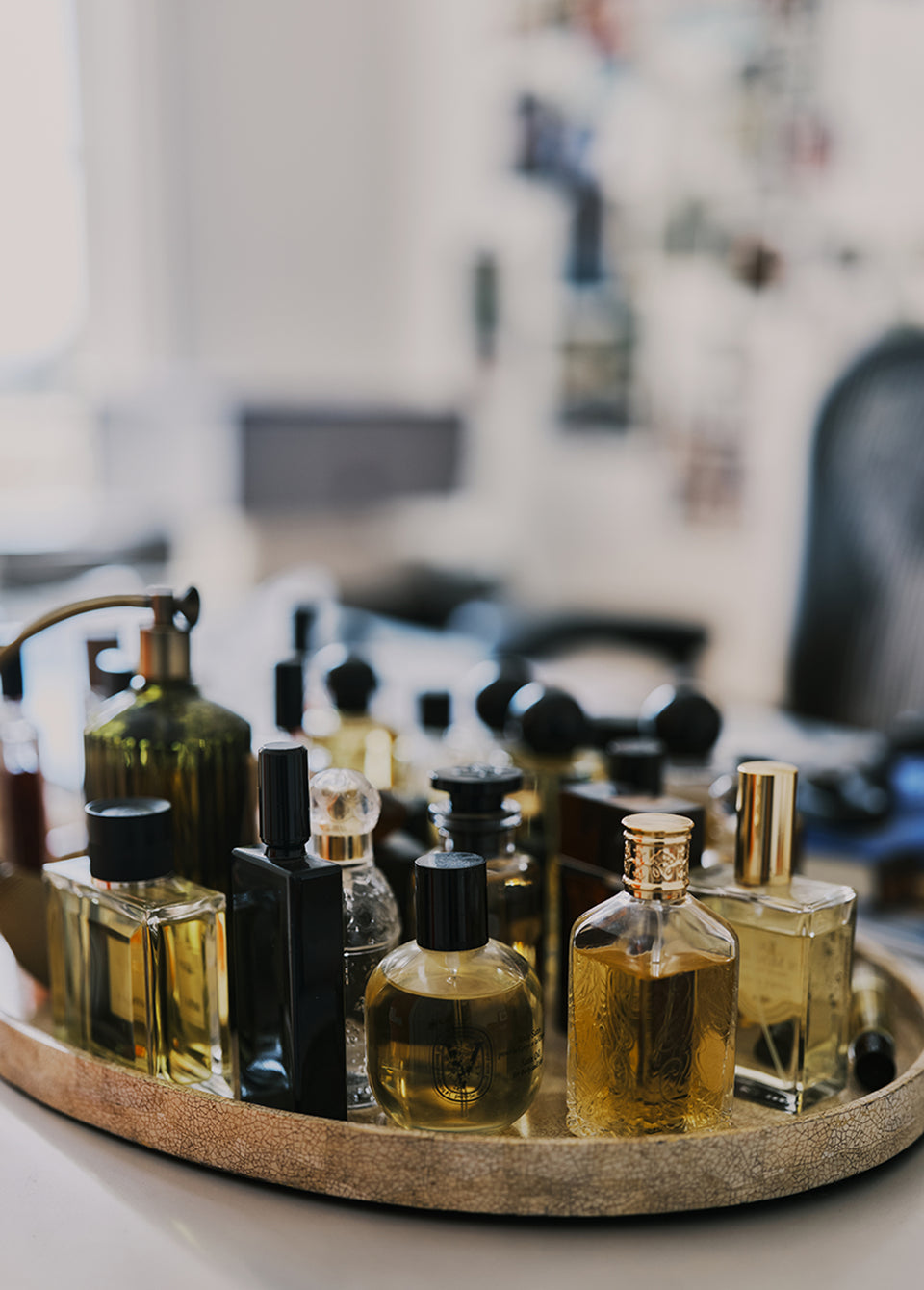 A collection of assorted perfume and oil bottles in various glass shapes and colors, including amber, green, and black, arranged on a round gold tray.