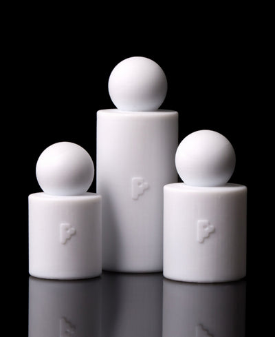 Three matte white silicone cylindrical holders with spherical tops, arranged in a pyramid-like grouping on a reflective black surface against a black background.