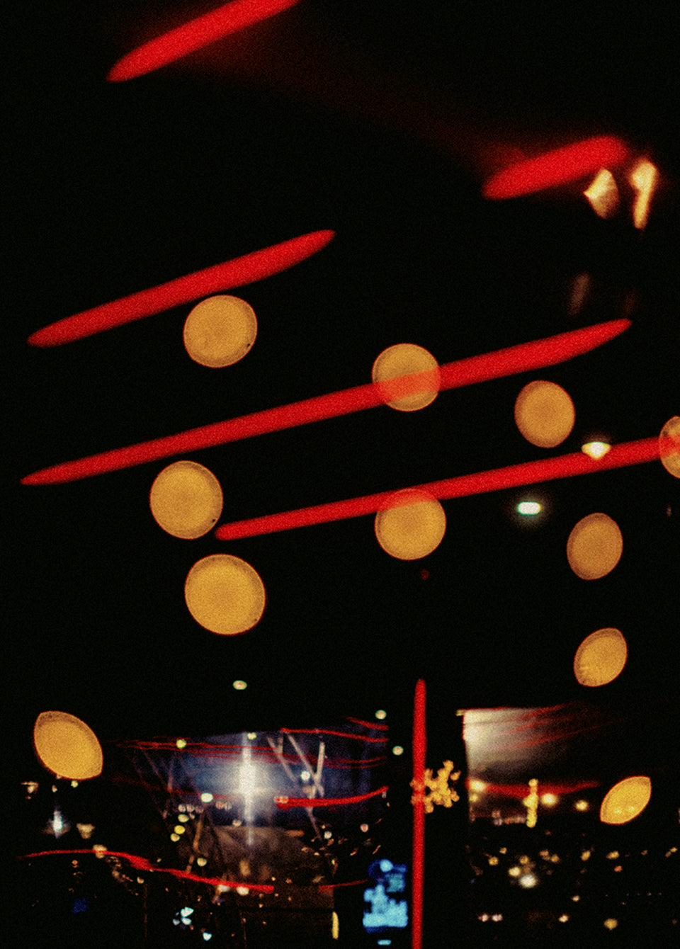Abstract photograph of hanging circular light fixtures glowing red and yellow against a dark night sky, with blurred city lights below.