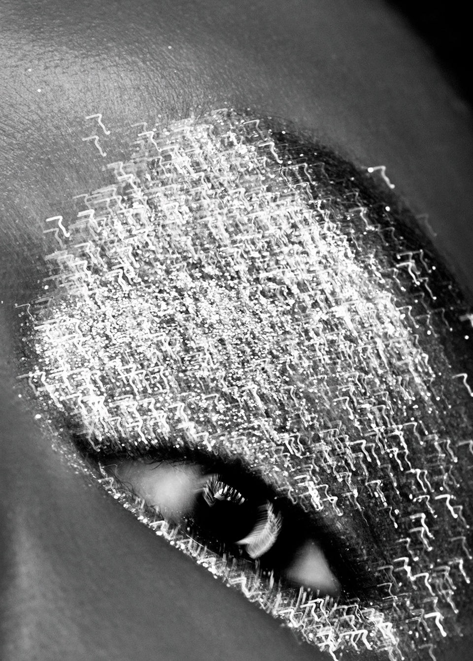 Black and white close-up of a human eye with dramatic metallic silver eyeshadow and textured shimmer across the eyelid and surrounding skin.