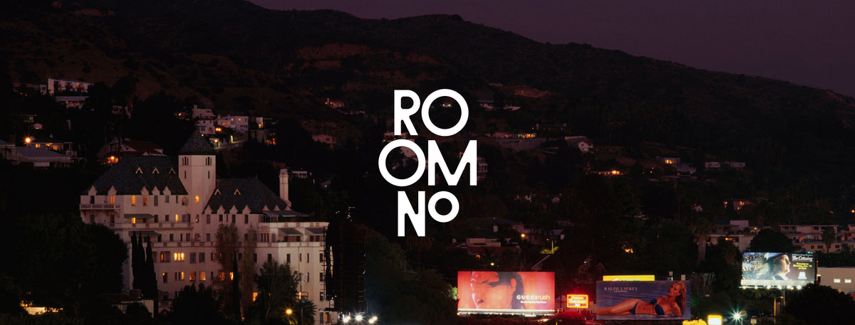 A dark nighttime cityscape with hills, buildings, and bright white vertical text reading 'ROOM NO' centered over the scene.