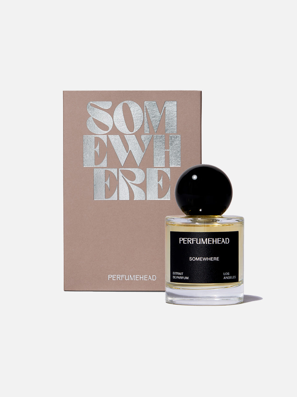 Perfumehead 'SOMEWHERE' fragrance bottle with pale yellow liquid and a black spherical cap, shown next to its beige box with metallic silver lettering, on a light gray background.