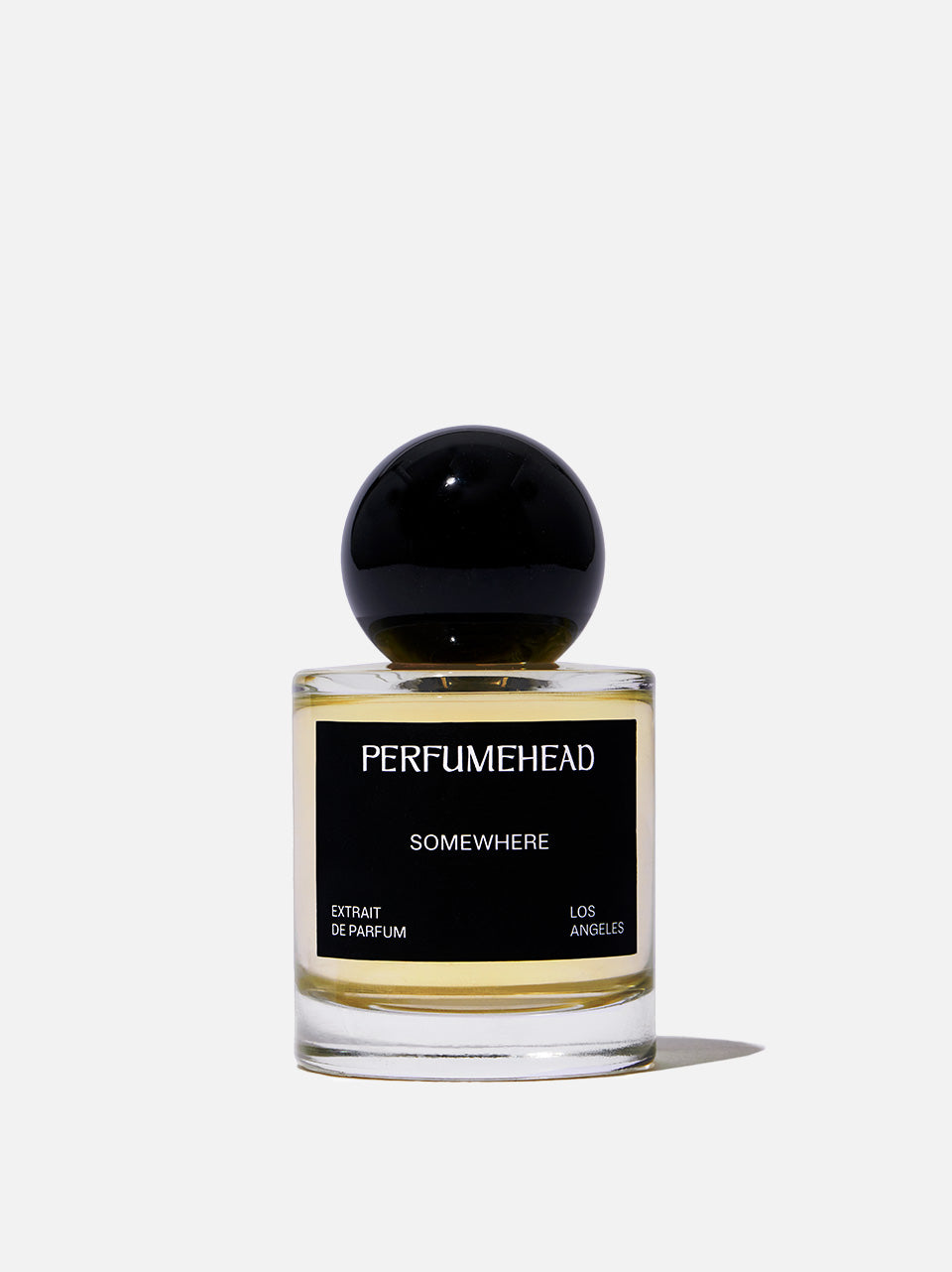 A bottle of Perfumehead 'SOMEWHERE' extrait de parfum, featuring a clear glass bottle with a black spherical cap and a black label with white text, set against a light gray background.
