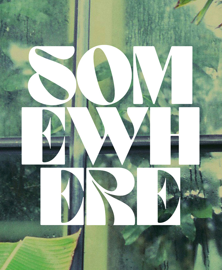 Large white typographic text reading 'SOMEWHERE' over a blurred green outdoor scene with window-like lines and foliage.