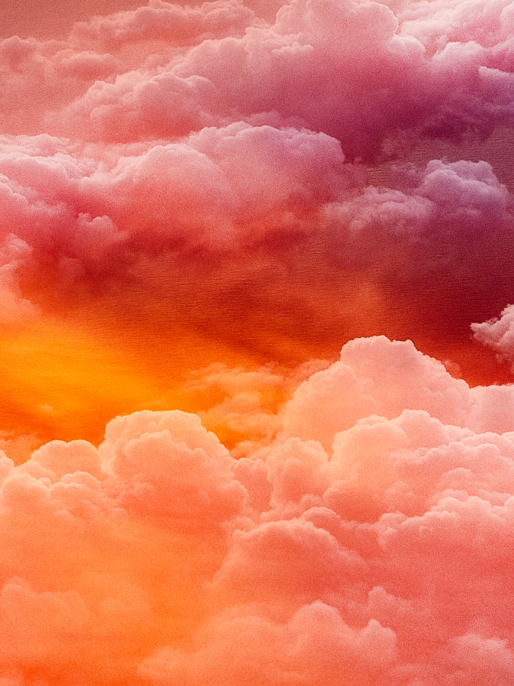 A dramatic sky scene filled with voluminous clouds in warm sunset tones, including pink, coral, orange, and deep red-purple shadows.